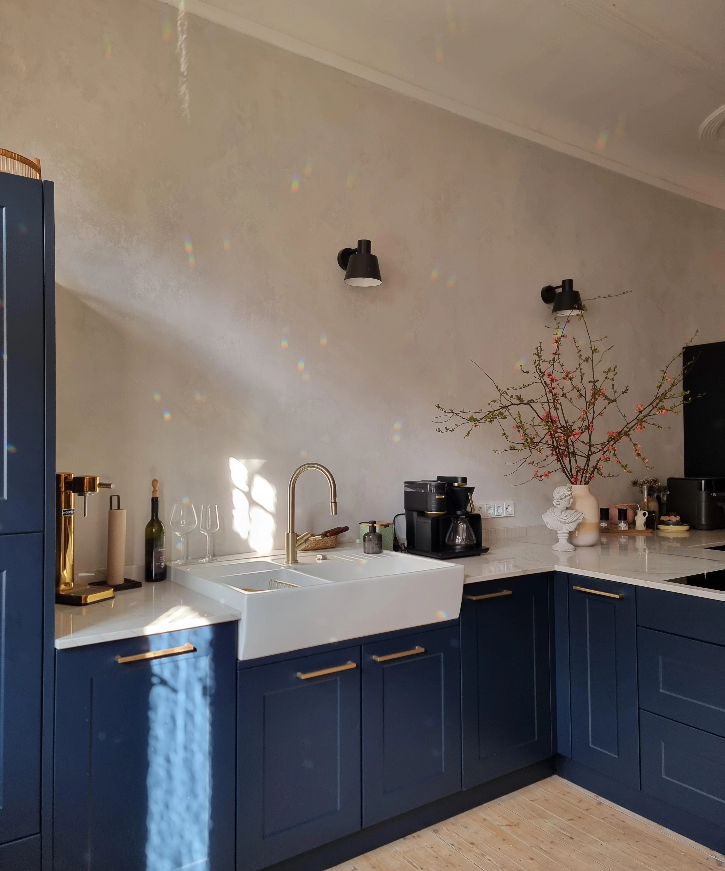 Une cuisine moderne avec des armoires bleues et des accents dorés, éclairée par la lumière du soleil. Nolte Kitchen.