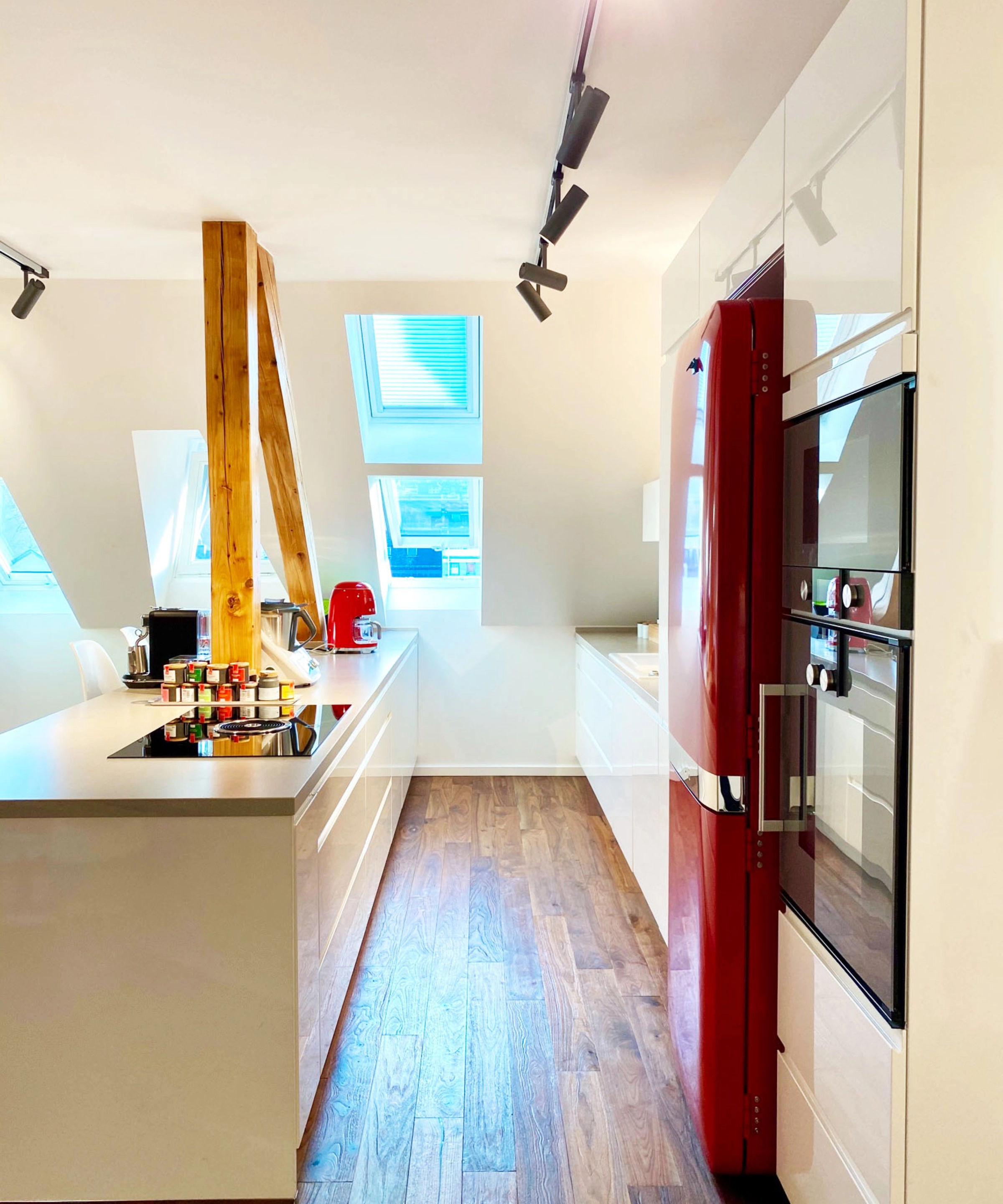 Une cuisine moderne avec des accents rouges et des éléments en bois, éclairée par des fenêtres de toit. Nolte Kitchen.