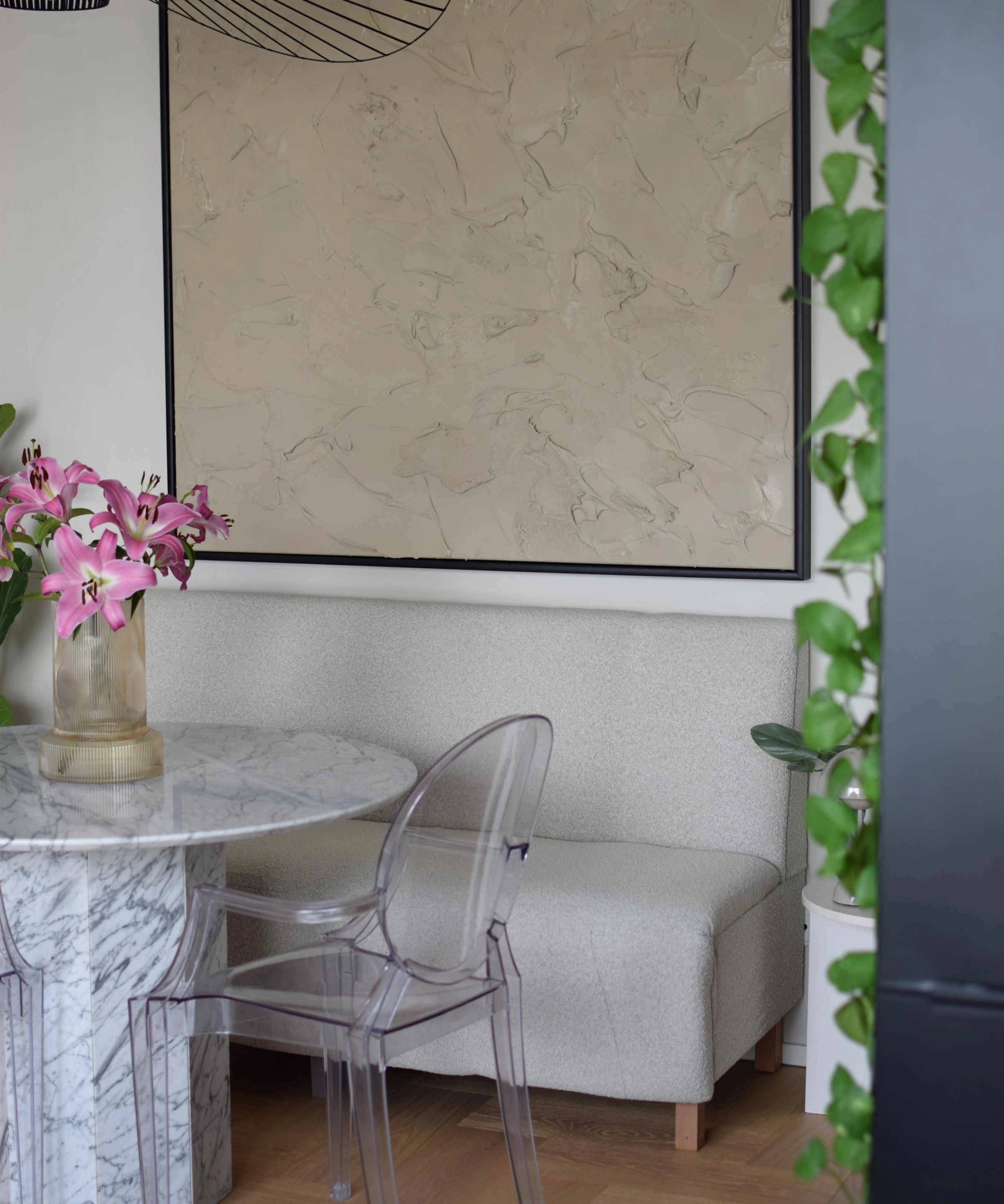 Salle à manger élégante avec table en marbre, fleurs, chaises transparentes, entourée de plantes. Nolte Living.