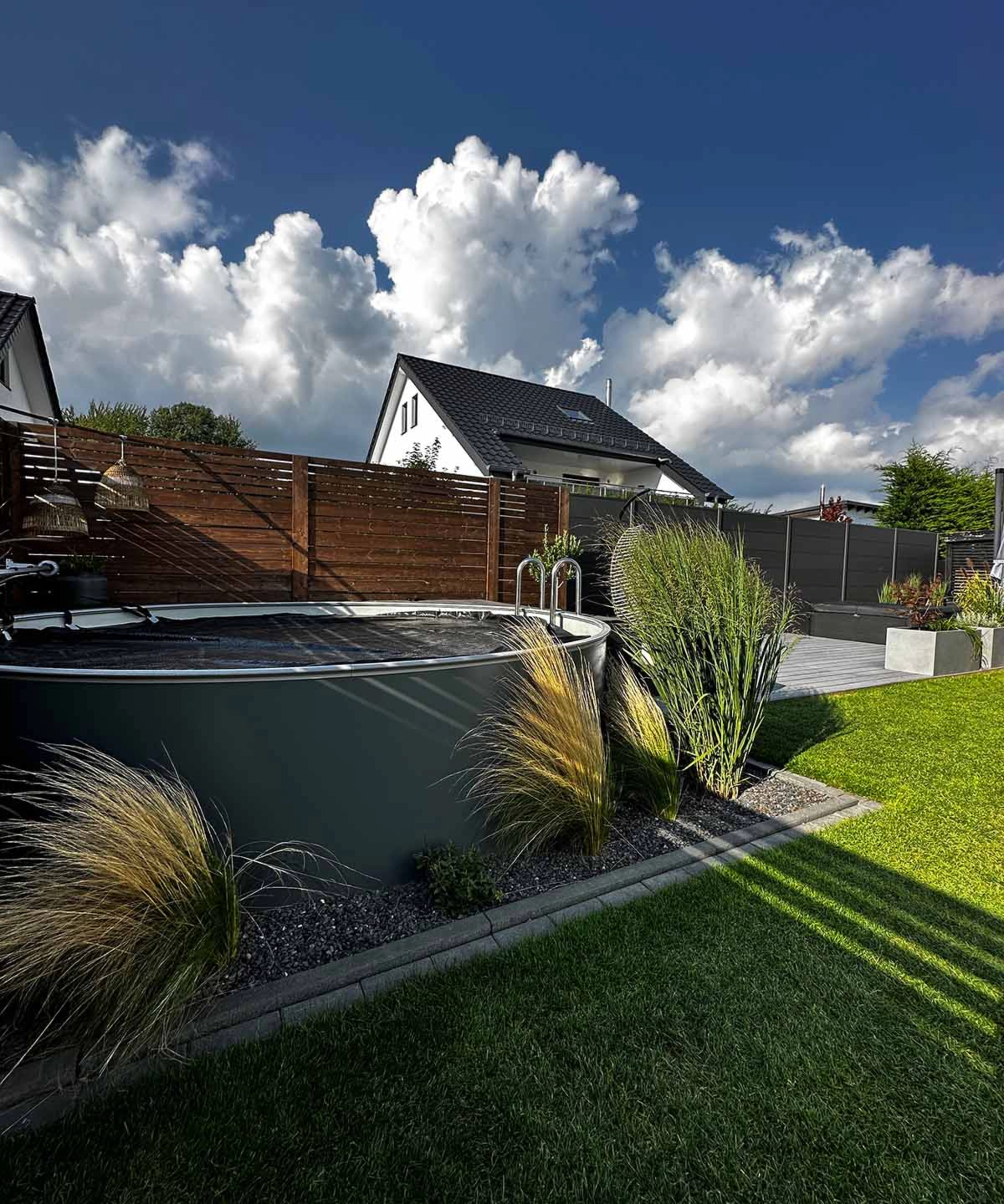 Un jardin moderne avec pelouse, graminées ornementales et une petite piscine sous un ciel bleu.