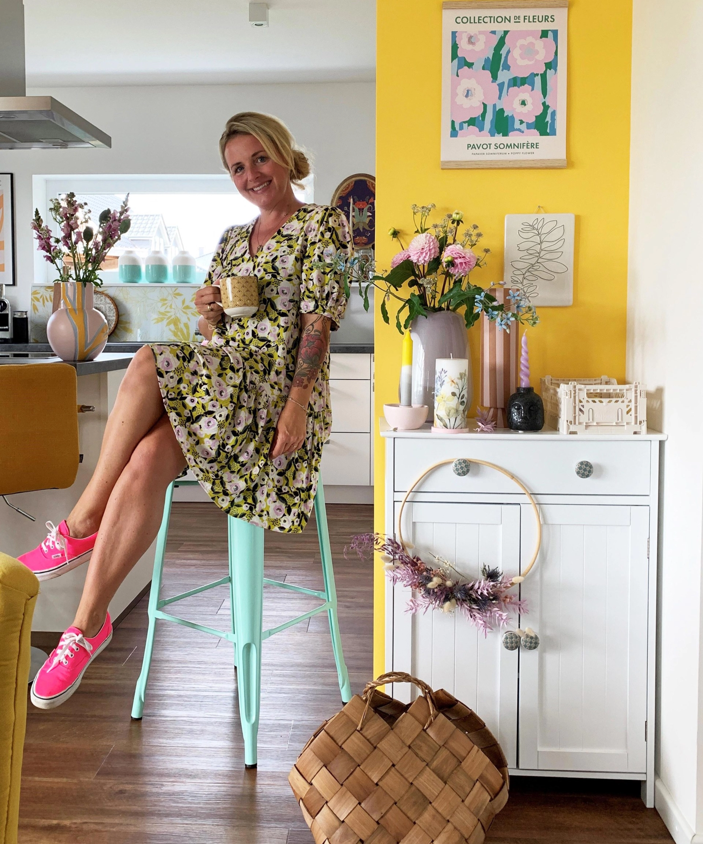 A woman sits in a cheerfully decorated Nolte kitchen, sipping from a cup.