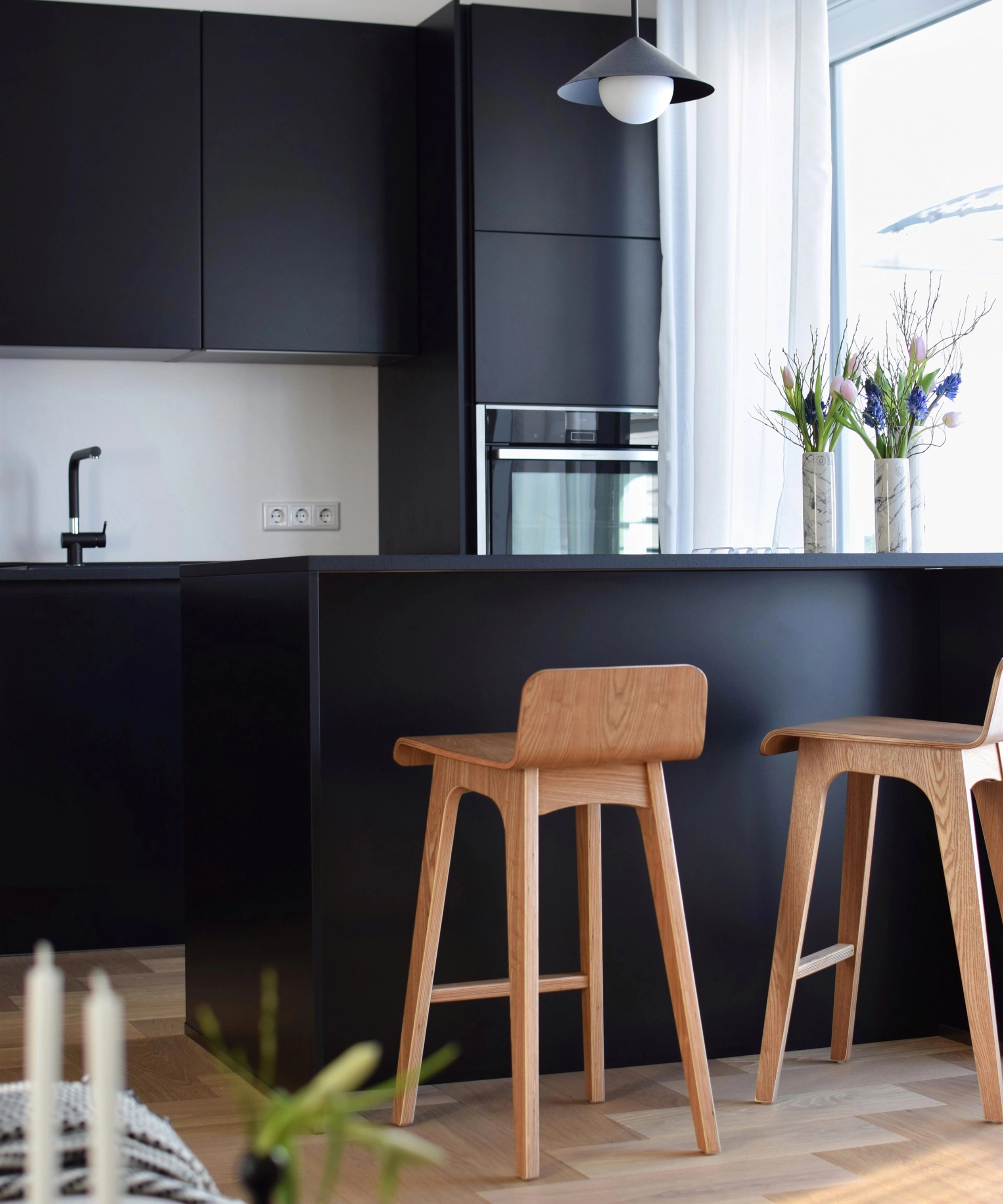 Cuisine moderne avec armoires noires et chaises en bois, conçue par Nolte Kitchen.