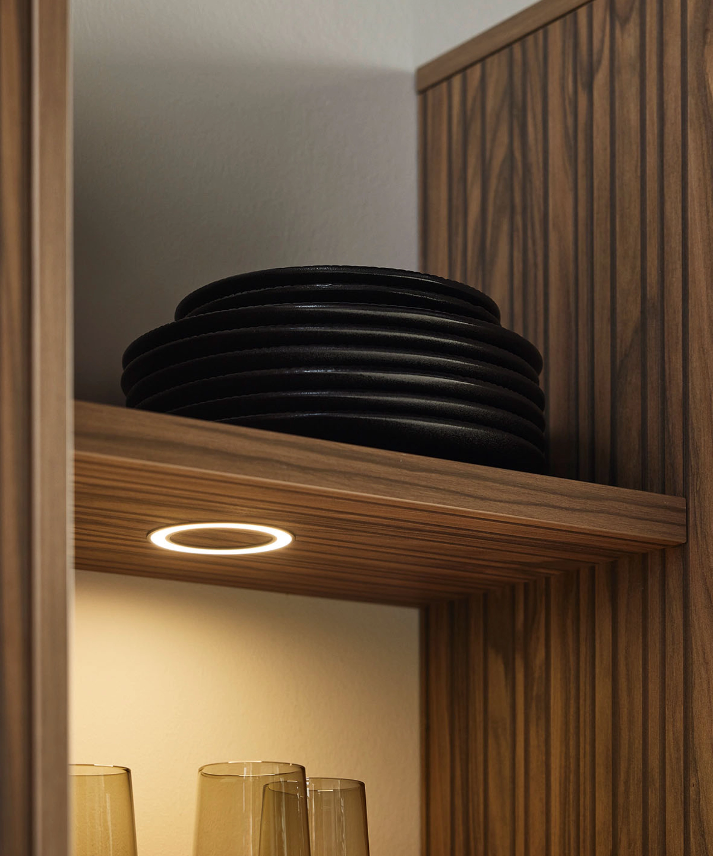 Ein Regal mit schwarzen Tellern und Gläsern in einem stilvollen Design von Nolte Living.