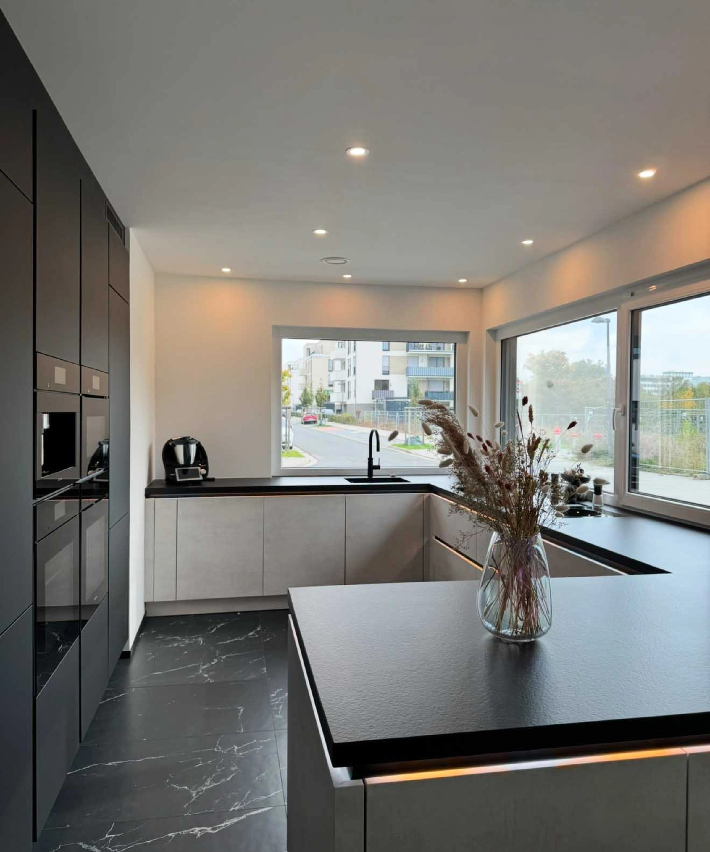 Une cuisine moderne avec des plans de travail noirs et de grandes fenêtres, conçue par Nolte Kitchen.