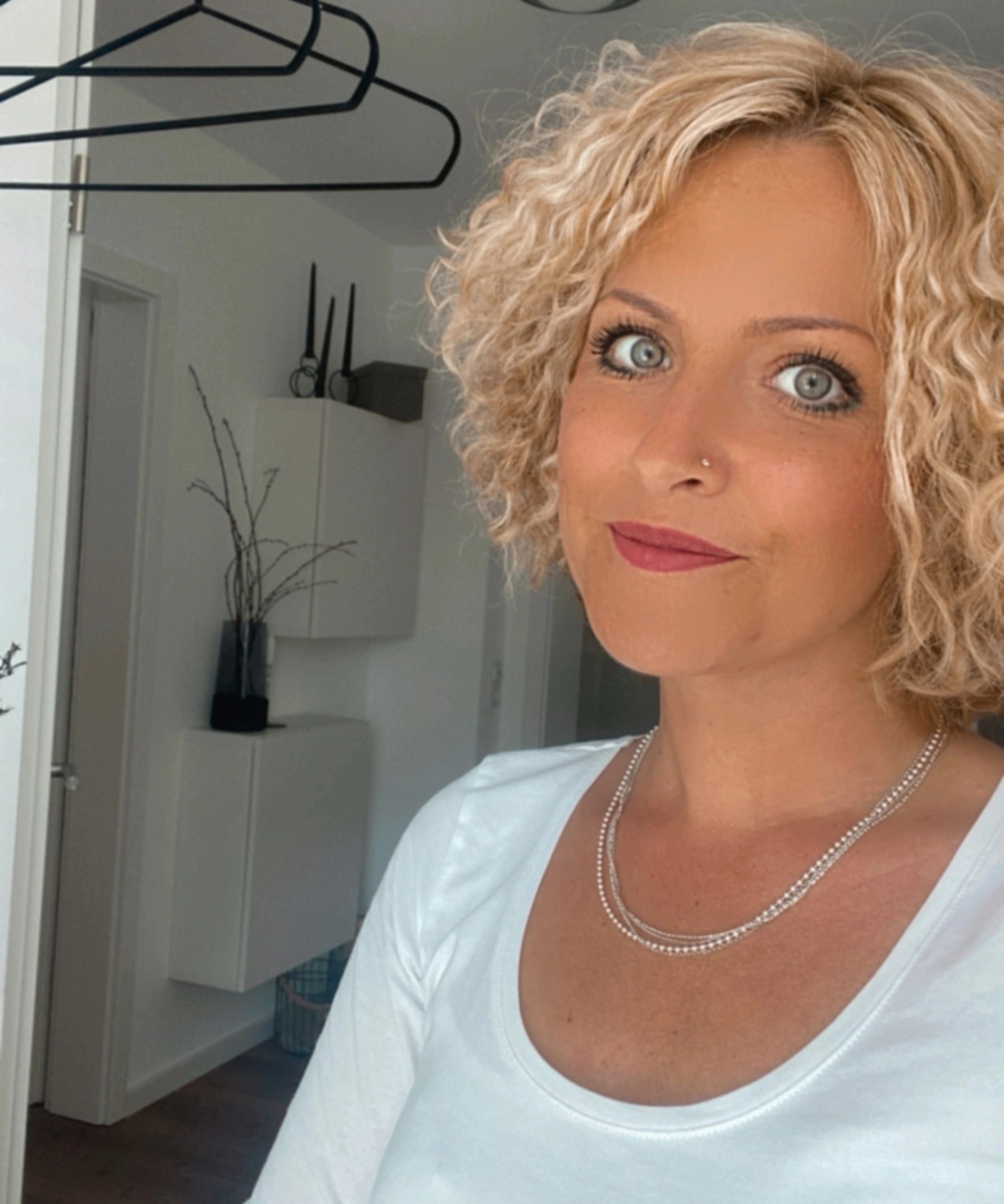 Une femme aux cheveux blonds bouclés se tient dans une pièce au décor moderne.
