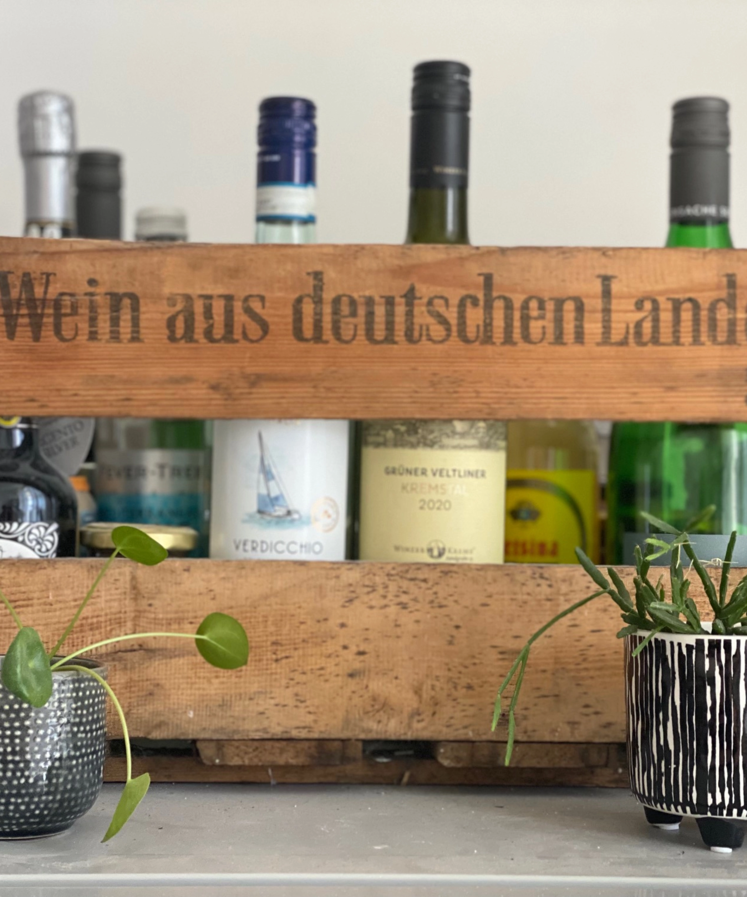 Une caisse en bois avec des bouteilles et des plantes crée une ambiance élégante, idéale pour les cuisines Nolte.