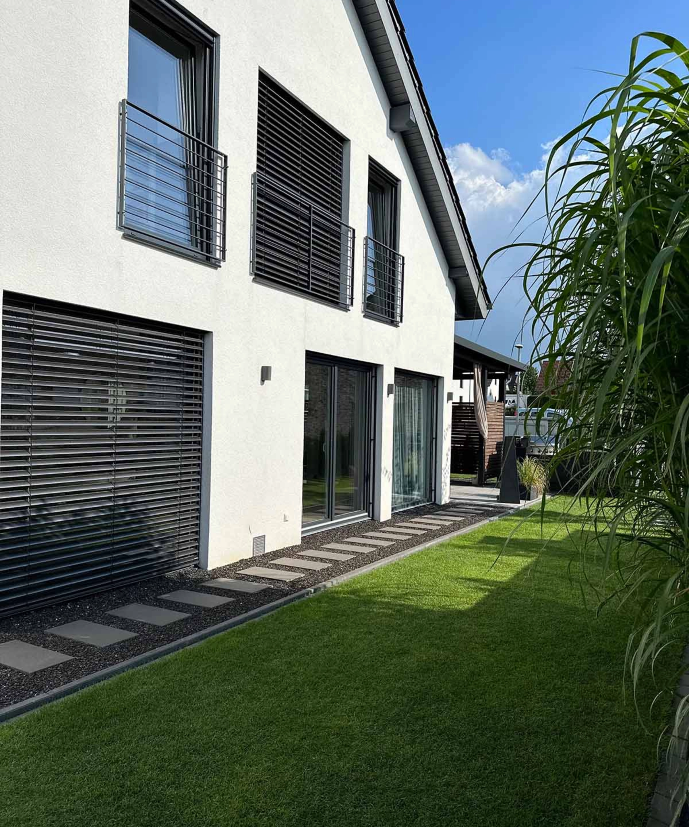 Une maison moderne avec de grandes fenêtres et une pelouse soignée par une journée ensoleillée.