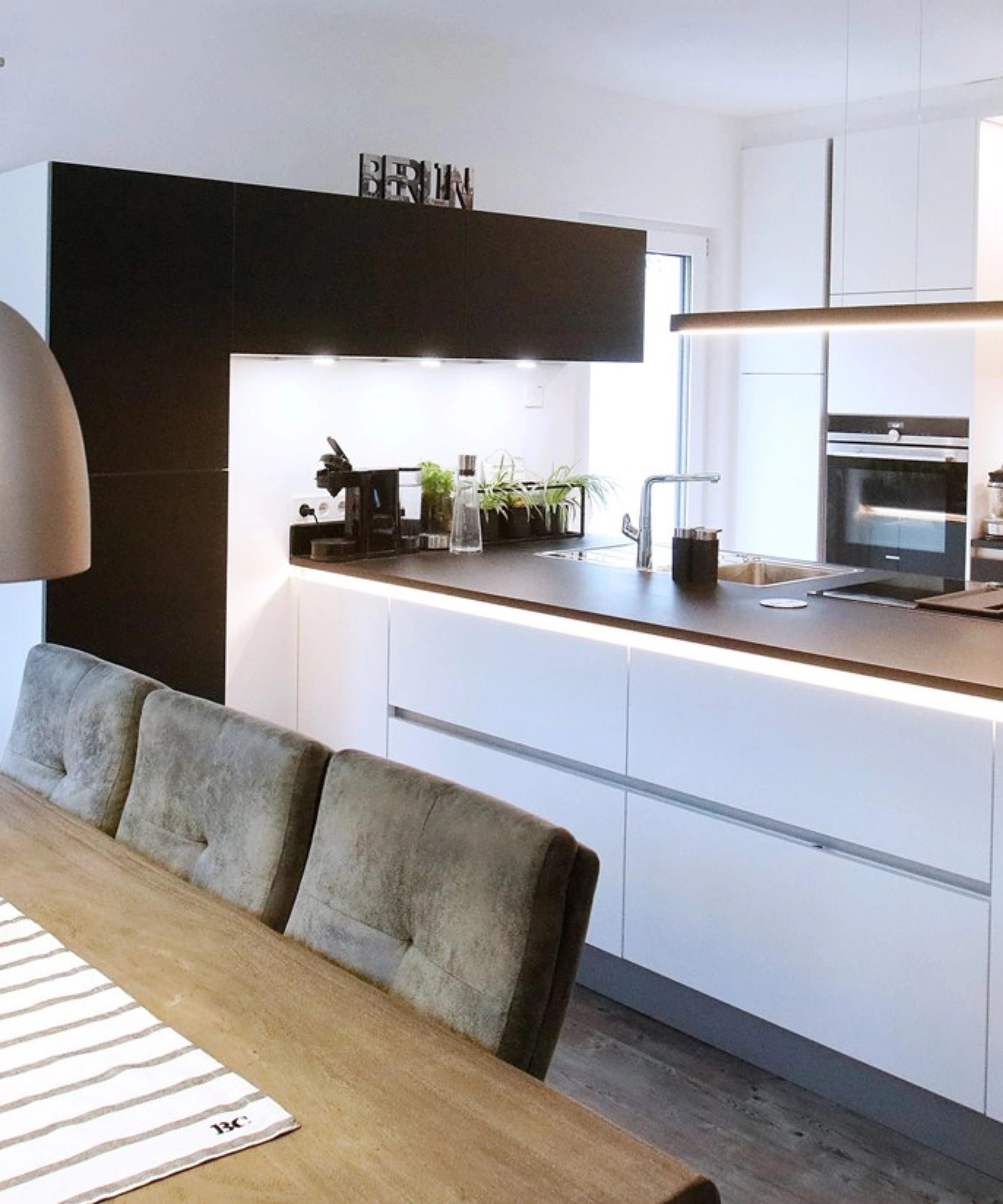 Cucina moderna con tavolo da pranzo e lampade a sospensione, presentata da Nolte Kitchen.