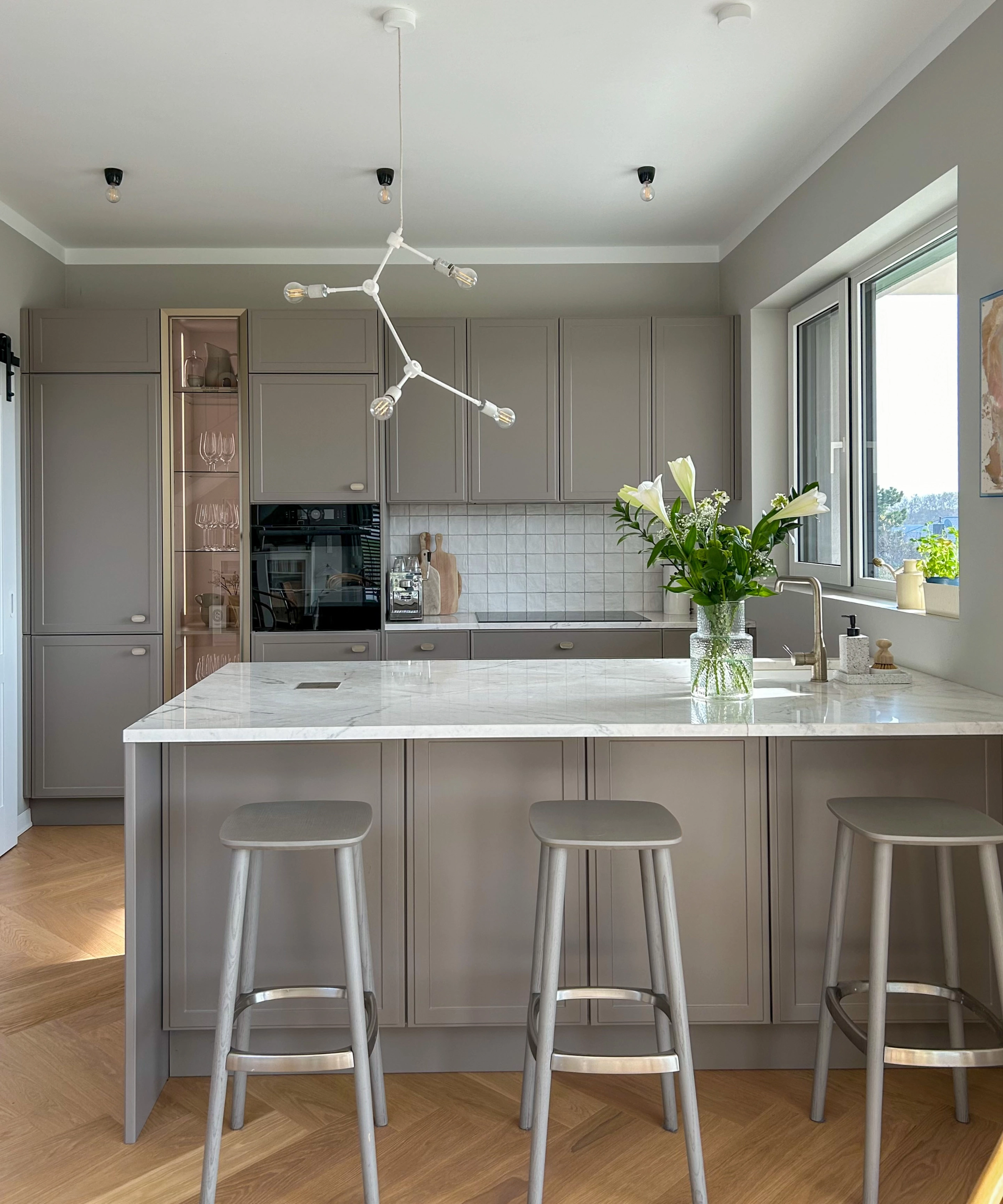 Une cuisine moderne avec des armoires grises et un îlot, décorée de fleurs. Nolte Kitchen.