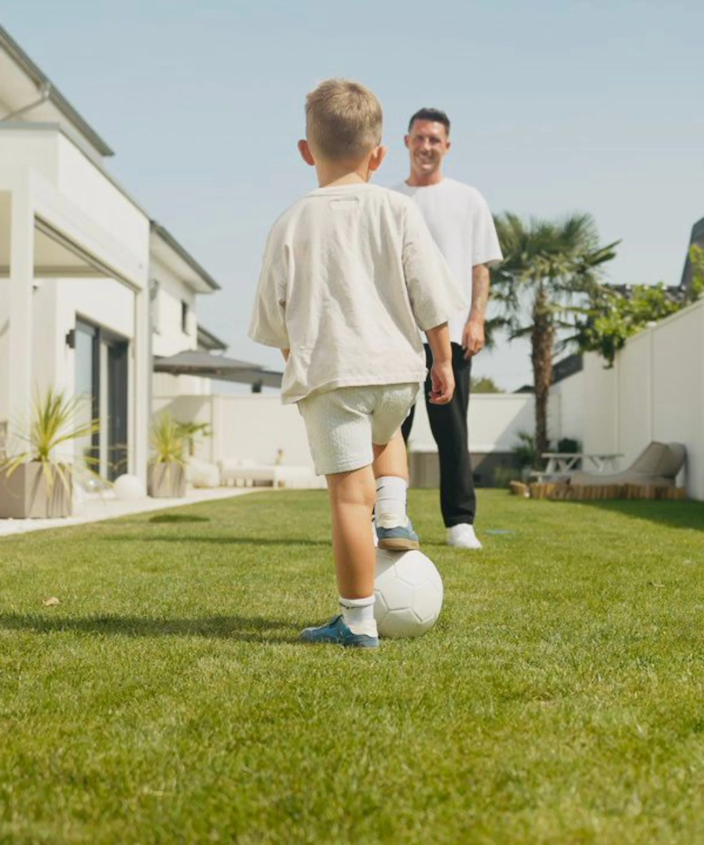 Un enfant joue au football avec un adulte dans le jardin.