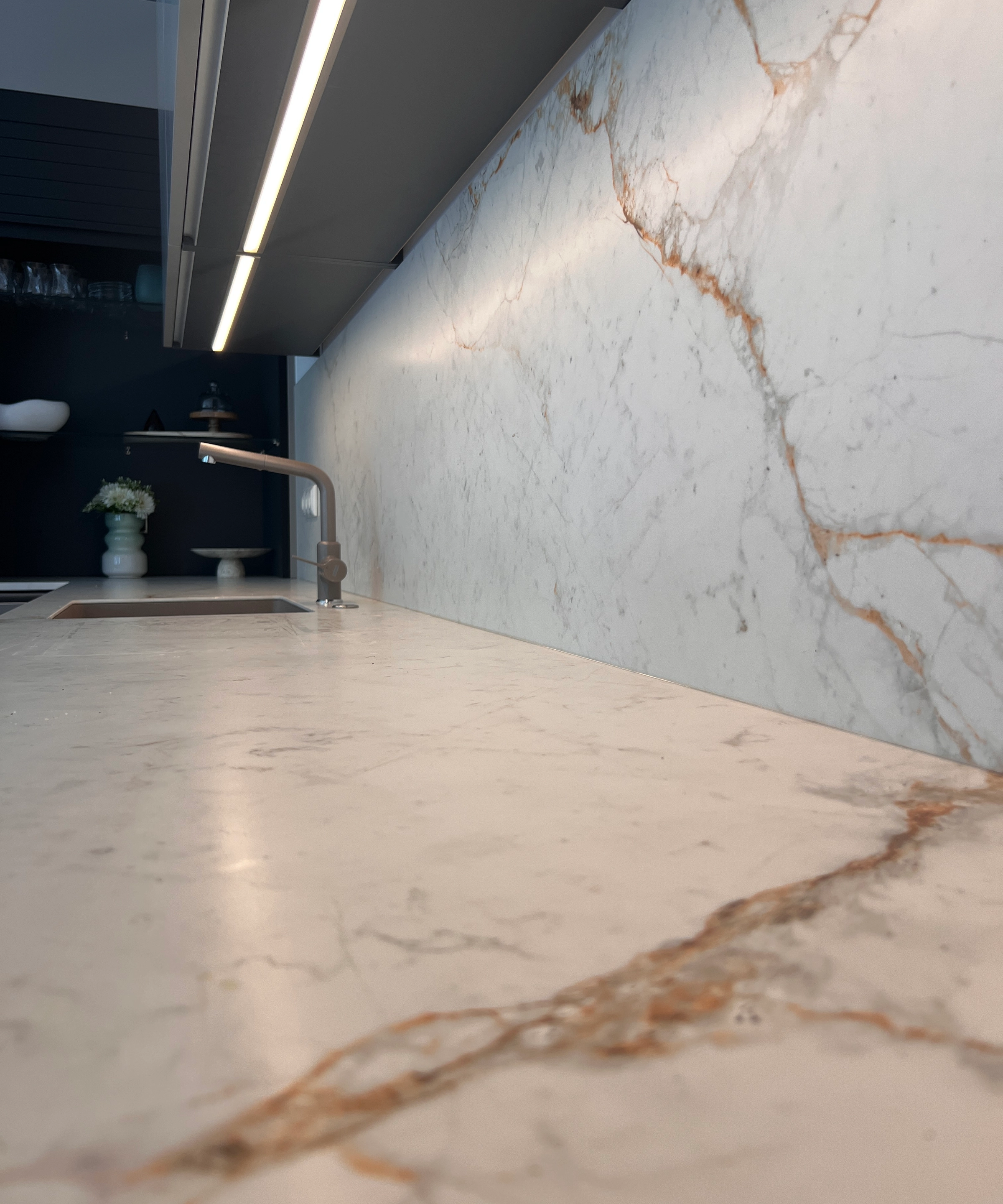 Cuisine moderne avec plan de travail en marbre et évier, éclairée par une lampe sous meuble. Nolte Kitchen.