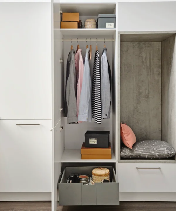 Une armoire ouverte avec vêtements et étagères, à côté une alcôve avec siège. Nolte Living.