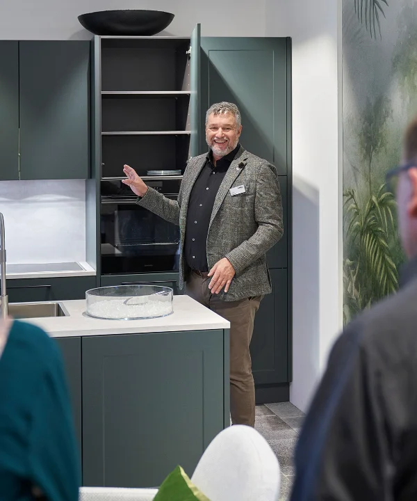 Osoba prezentuje nowoczesną kuchnię z ciemnymi szafkami i białym blatem. Nolte Kitchen.