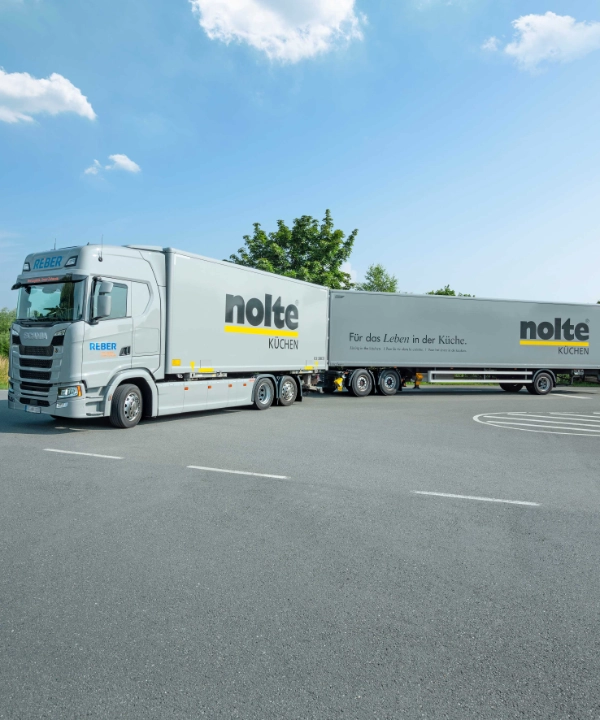 Un camion avec l'inscription "Nolte Kitchen" est garé sur un parking sous un ciel bleu.
