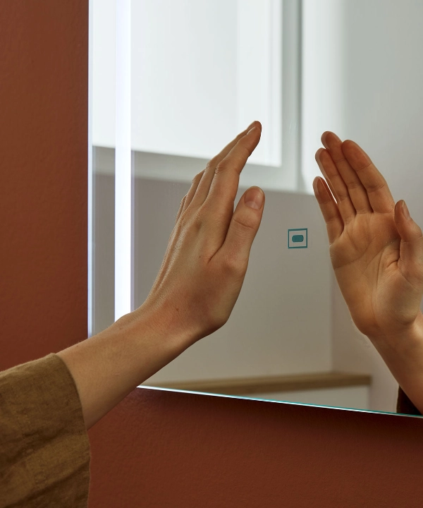 Een hand raakt een verlichte spiegel aan in een modern badkamer, Nolte SPA.